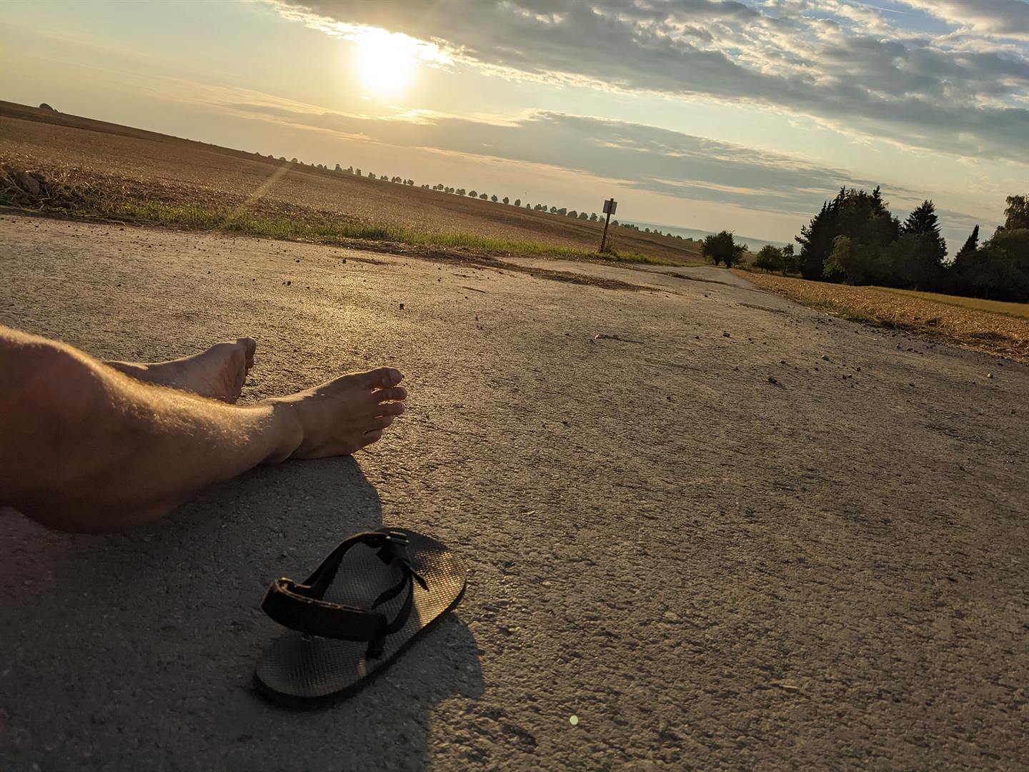 Barfüße und eine Sandale liegen auf einem Feldweg bei Sonnenuntergang während einer Laufpause