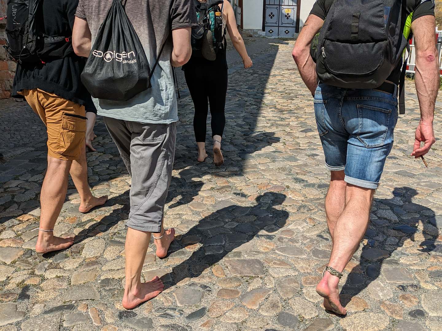 Eine Gruppe geht barfuß über Kopfsteinpflaster durch eine Altstadt