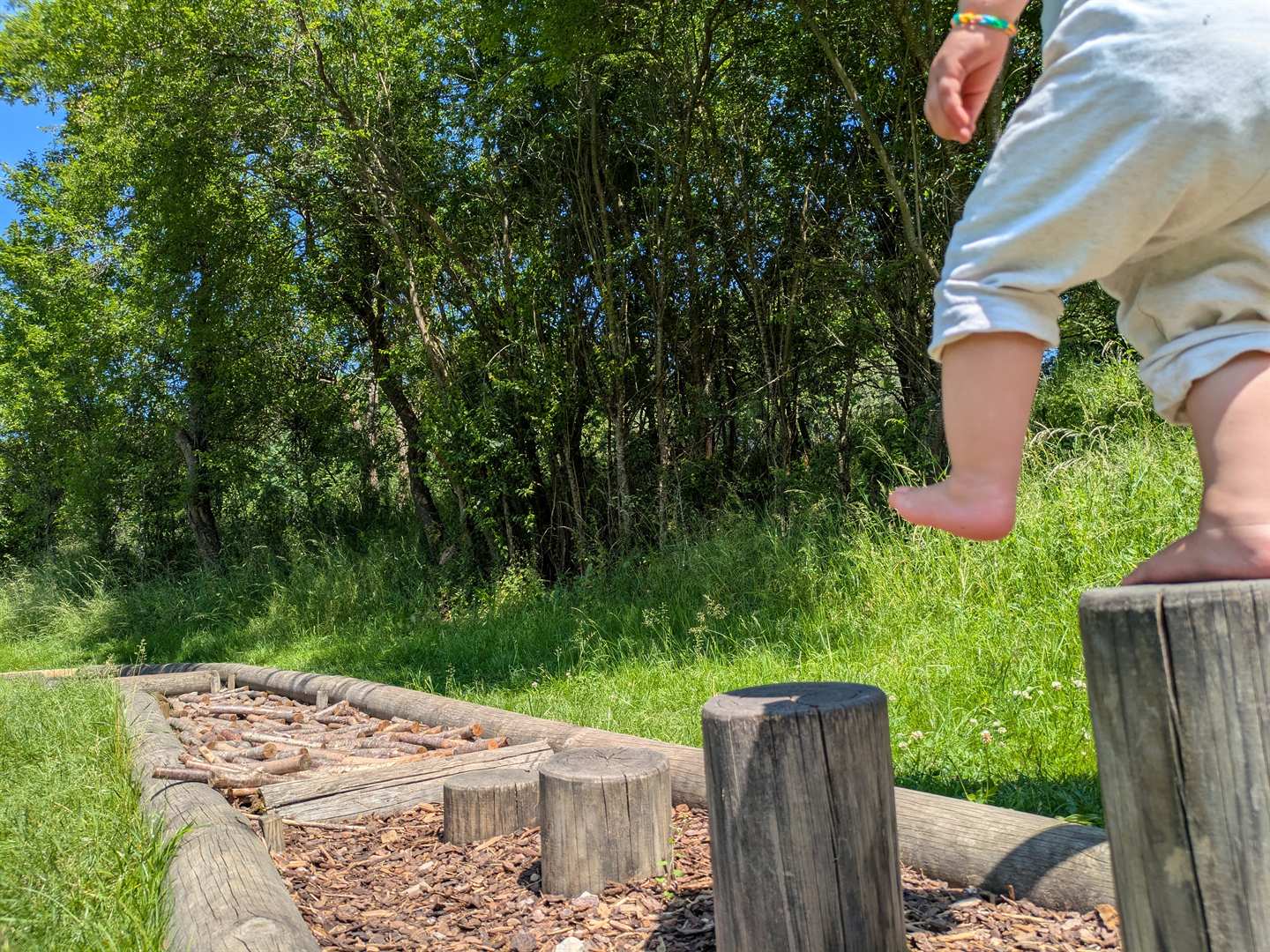 Ein kleines Kind balanciert barfuß auf den Holzstämmen eines Barfußpfads