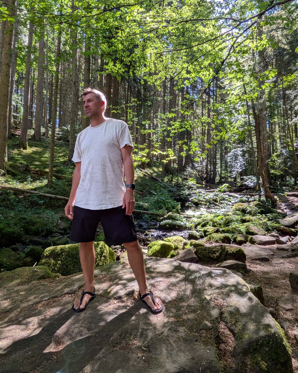 Stefan Siemroth steht in Barfußsandalen auf einem moosbewachsenen Felsen im Wald