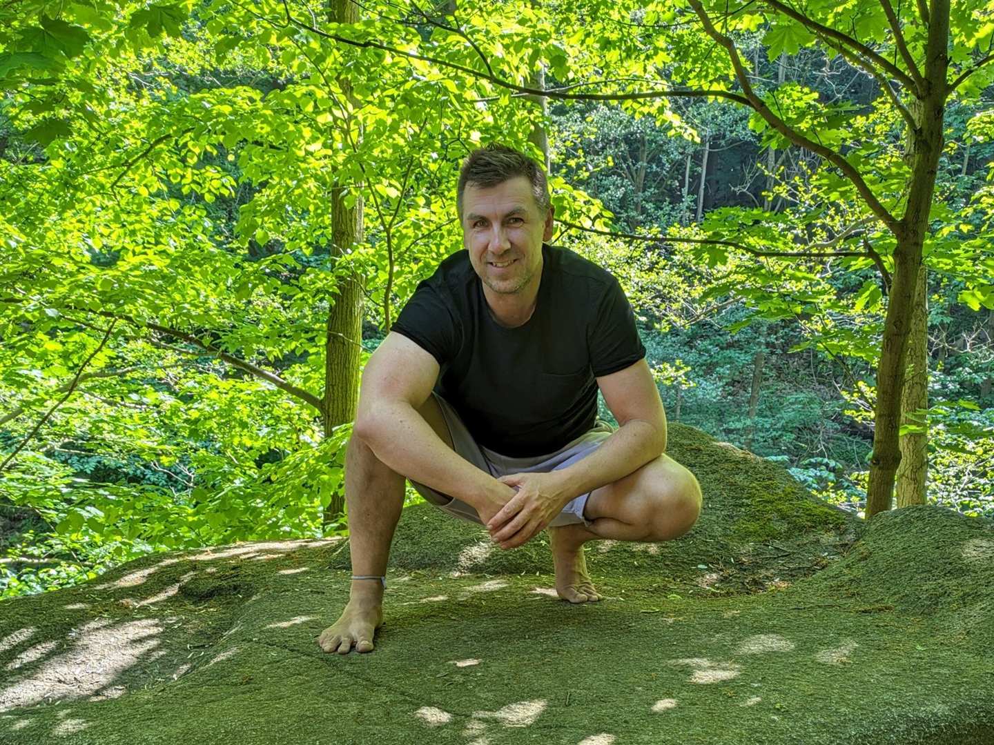 Stefan Siemroth hockt barfuß auf einem Felsen im Wald und lächelt in die Kamera